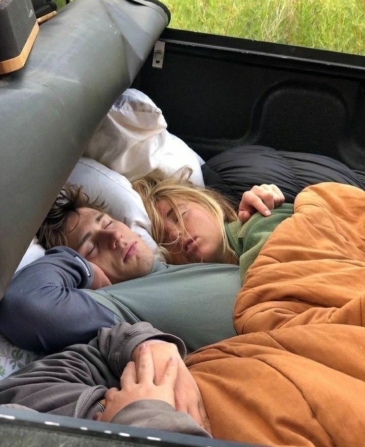 Two people asleep in sleeping bags in the back of a truck.