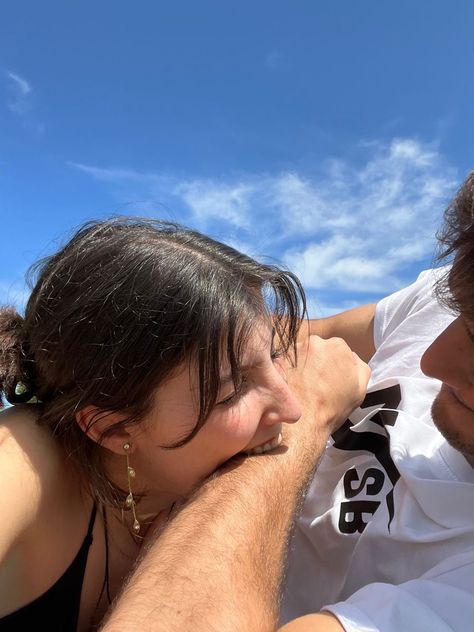 A person lying with their head resting on someone's arm against a bright blue sky.