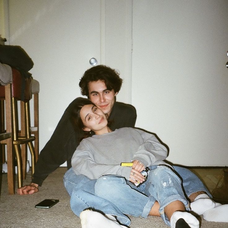 Two people sitting on the floor leaning back against a sofa.