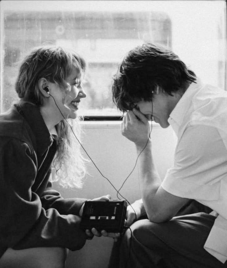 A black and white photograph of two people sitting together sharing headphones.