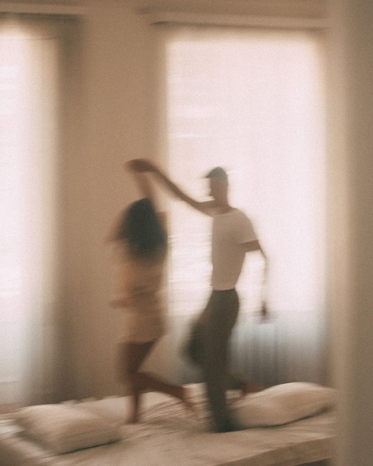 A long-exposure photograph of two people dancing in a bright bedroom.