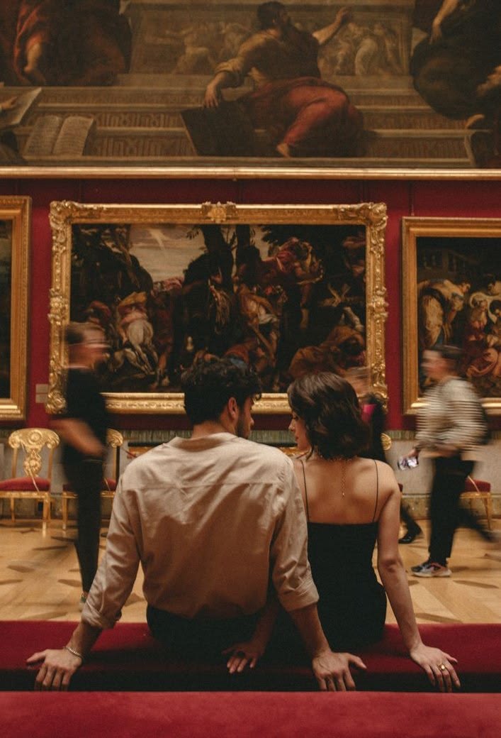 People in front of a large painting in a gallery, a long red bench in front of it.