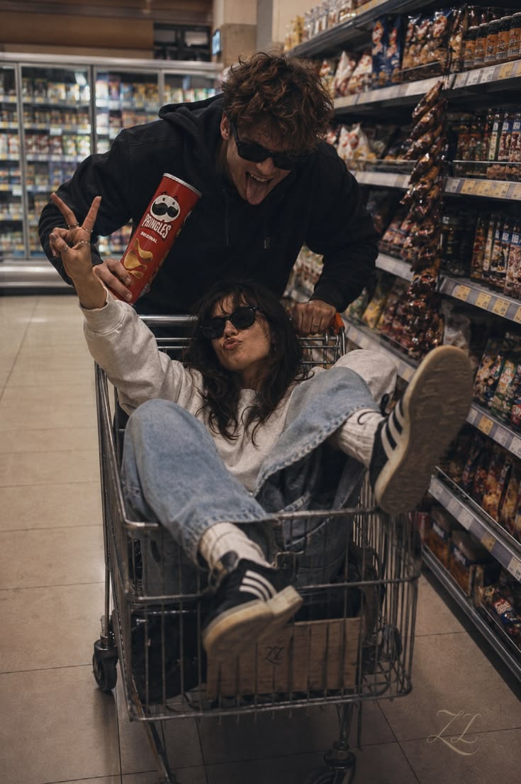 One person pushing a supermarket trolley with the other sitting inside it.