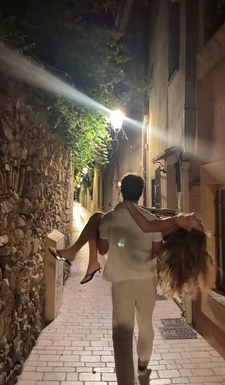 Two people in a narrow stone alley at night, a shaft of light falling between the walls.